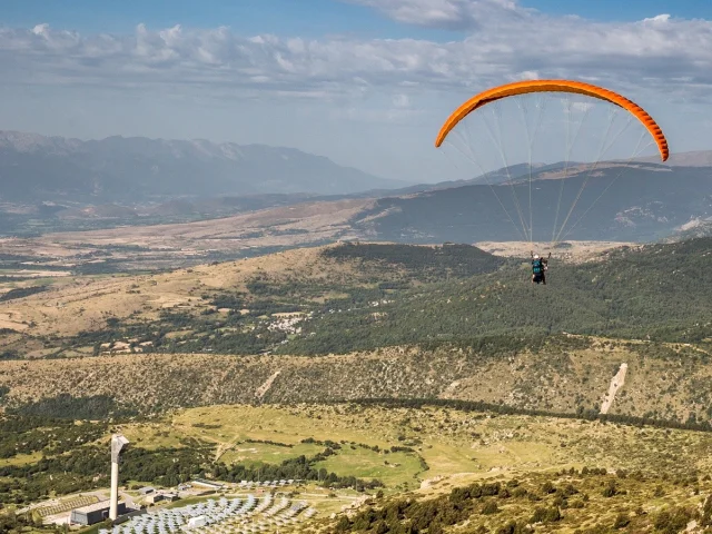 Parapentiste en vol au-dessus du Four Solaire d’Odeillo, avec vue sur les montagnes et la plaine de Cerdagne dans les Pyrénées-Orientales.