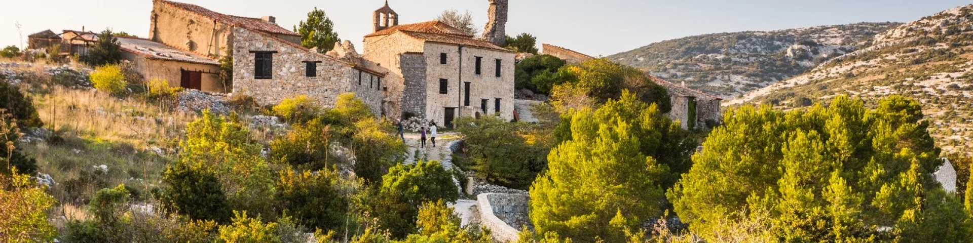 Vue du village en pierre de Périllos, perché sur les hauteurs et entouré de collines et de garrigue, baigné par la lumière dorée de fin d’après-midi.