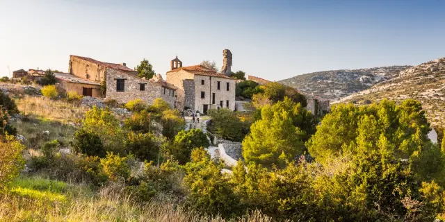 Vue du village en pierre de Périllos, perché sur les hauteurs et entouré de collines et de garrigue, baigné par la lumière dorée de fin d’après-midi.