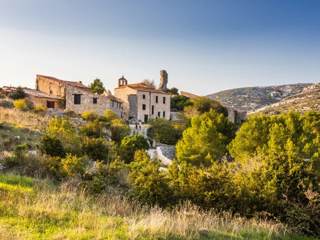 Vue du village en pierre de Périllos, perché sur les hauteurs et entouré de collines et de garrigue, baigné par la lumière dorée de fin d’après-midi.