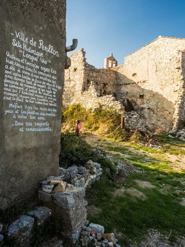 Vue du village en ruines de Périllos, site historique situé dans les Pyrénées-Orientales, avec un message d’accueil peint sur un mur invitant les visiteurs au respect du lieu.