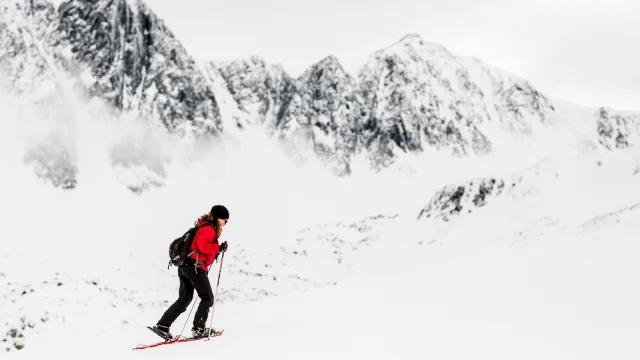 Randonneuse en raquettes progressant sur une pente enneigée face aux sommets escarpés des Pyrénées-Orientales.