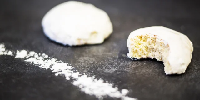 Deux rousquilles catalanes couvertes de glaçage blanc, posées sur une surface sombre saupoudrée de sucre glace, dont l’une est entamée.