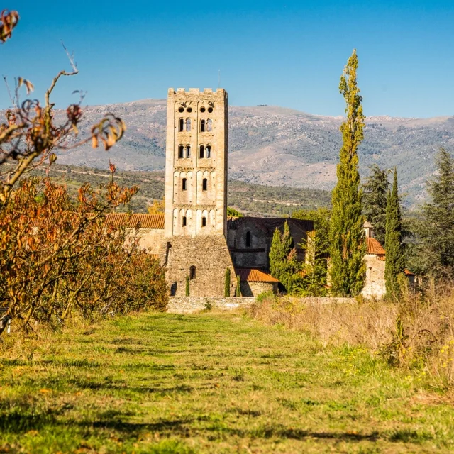 Abbaye romane Sainte-Marie d’Arles-sur-Tech entourée de vergers et de collines, sous un ciel bleu limpide.