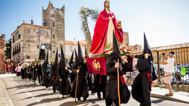 Participants de la Procession de la Sanch à Perpignan portant une statue du Christ vêtue de rouge, suivie d’autres pénitents en habits noirs dans les rues du centre-ville.
