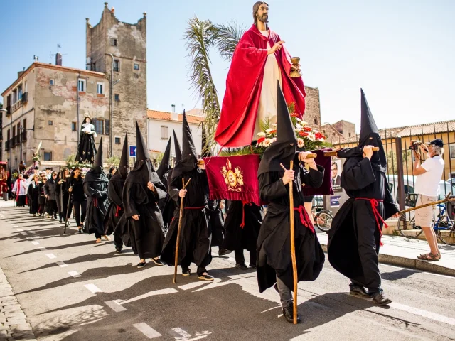 Participants de la Procession de la Sanch à Perpignan portant une statue du Christ vêtue de rouge, suivie d’autres pénitents en habits noirs dans les rues du centre-ville.