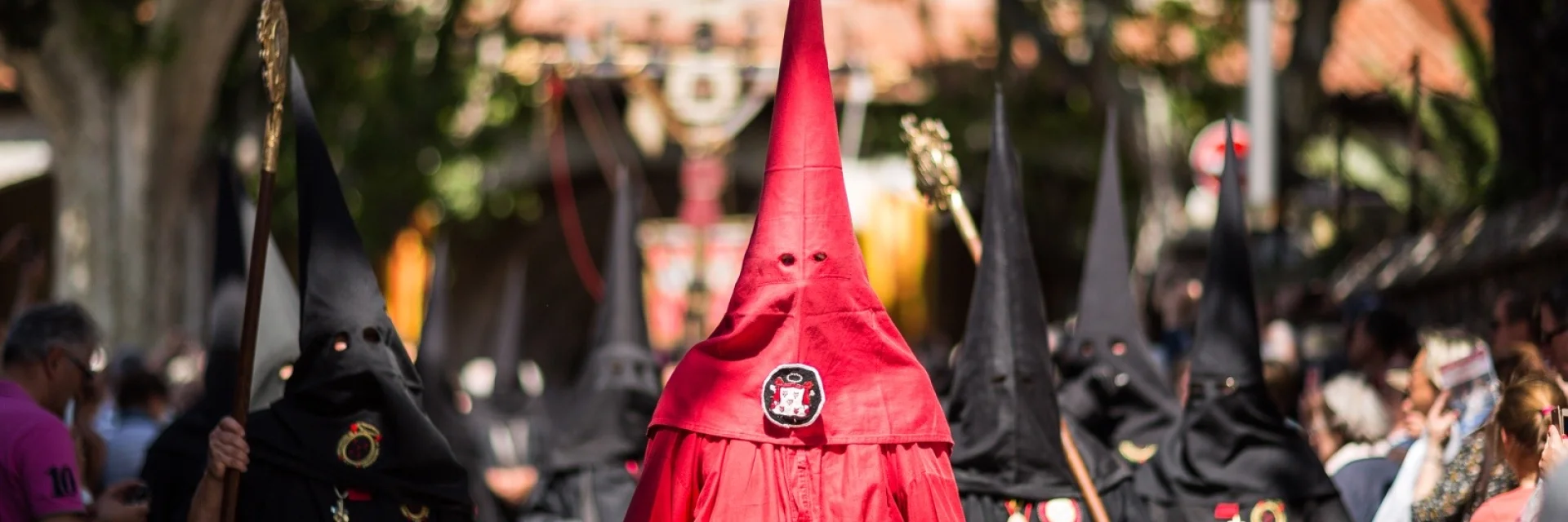 Pénitents vêtus de rouge et de noir défilant dans les rues de Perpignan lors de la Procession de la Sanch, sous le regard du public.