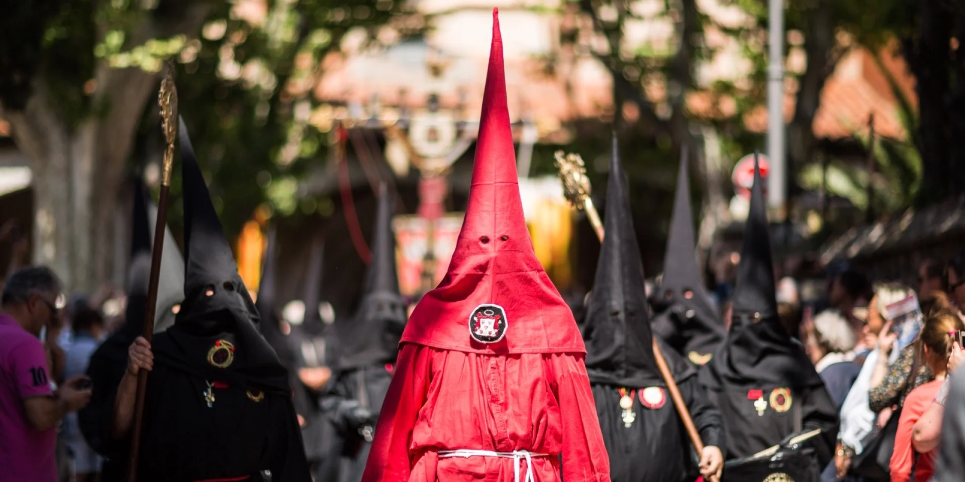 Pénitents vêtus de rouge et de noir défilant dans les rues de Perpignan lors de la Procession de la Sanch, sous le regard du public.