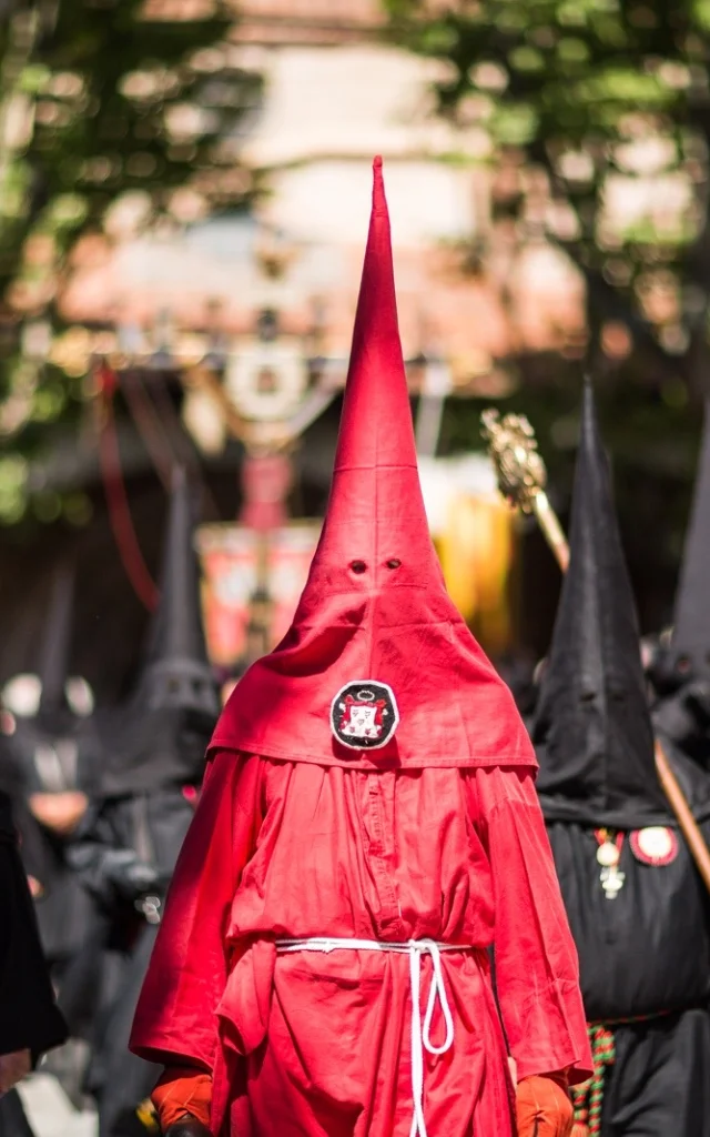 Pénitents vêtus de rouge et de noir défilant dans les rues de Perpignan lors de la Procession de la Sanch, sous le regard du public.