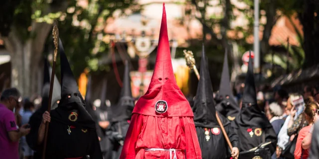 Pénitents vêtus de rouge et de noir défilant dans les rues de Perpignan lors de la Procession de la Sanch, sous le regard du public.