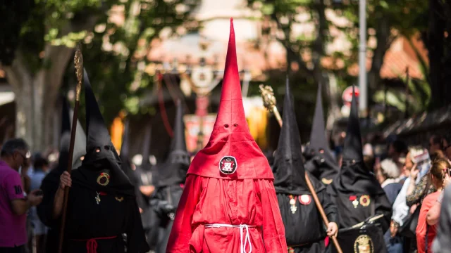 Pénitents vêtus de rouge et de noir défilant dans les rues de Perpignan lors de la Procession de la Sanch, sous le regard du public.