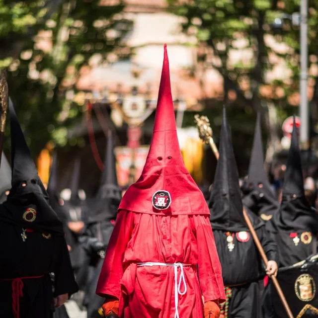 Pénitents vêtus de rouge et de noir défilant dans les rues de Perpignan lors de la Procession de la Sanch, sous le regard du public.