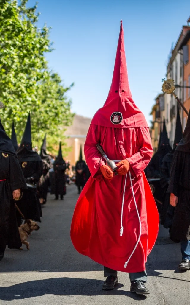Pénitents vêtus de noir et de rouge défilant dans les rues de Perpignan lors de la Procession de la Sanch, sous le regard du public rassemblé.