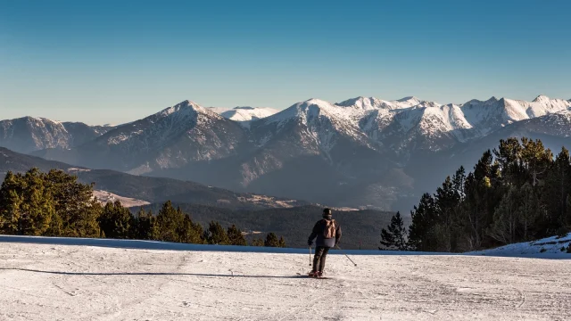 Skieur descendant une piste enneigée avec vue panoramique sur les montagnes du massif du Canigó dans les Pyrénées catalanes.