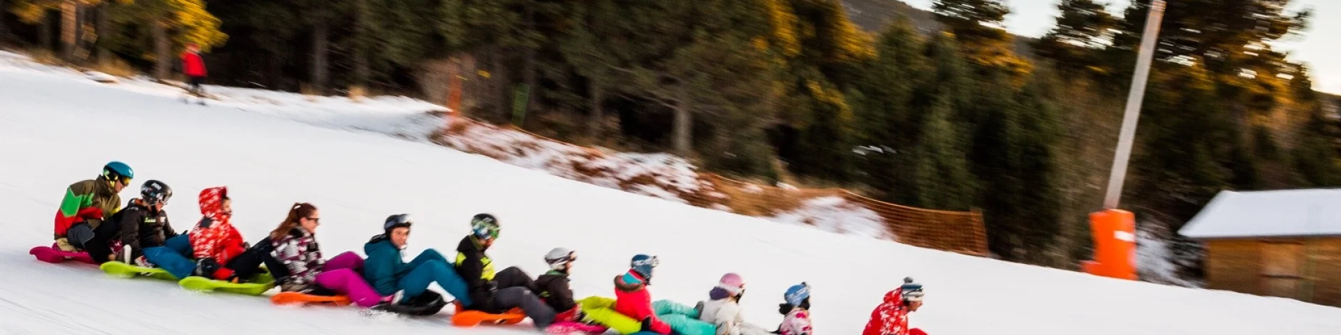 Activité snake glissGroupe de personnes descendant une piste enneigée en luge accrochées les unes aux autres, dans une ambiance conviviale à la montagne.