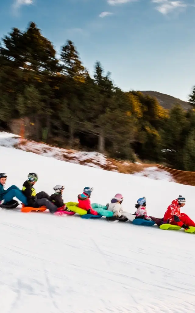 Activité snake glissGroupe de personnes descendant une piste enneigée en luge accrochées les unes aux autres, dans une ambiance conviviale à la montagne.