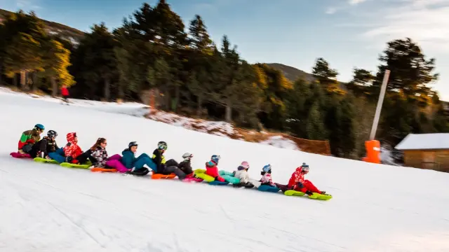 Activité snake glissGroupe de personnes descendant une piste enneigée en luge accrochées les unes aux autres, dans une ambiance conviviale à la montagne.