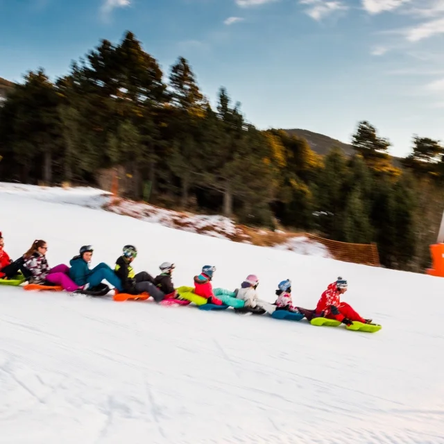 Activité snake glissGroupe de personnes descendant une piste enneigée en luge accrochées les unes aux autres, dans une ambiance conviviale à la montagne.