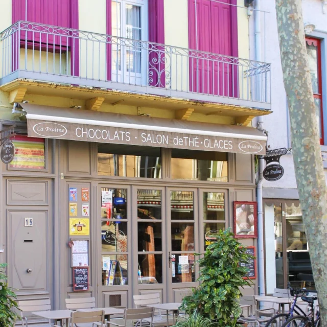 Façade colorée du salon de thé et chocolaterie La Praline à Céret, avec terrasse ombragée et volets pourpres typiques du centre historique.