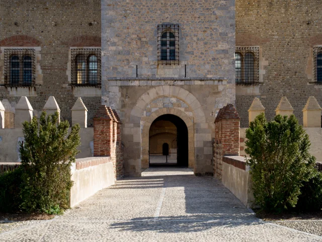 Entrée voûtée du Castillet à Perpignan, bâtie en pierre et en brique, avec ses fenêtres grillagées et son passage central éclairé par le soleil.