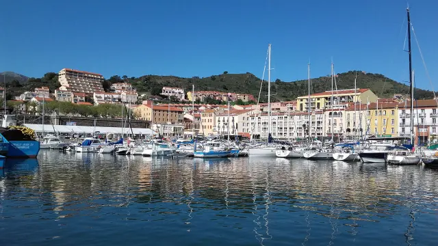 Vue du port de Port-Vendres avec ses voiliers amarrés et les façades colorées des bâtiments bordant le quai sous un ciel bleu.