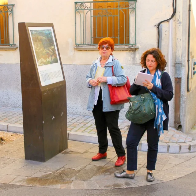 Deux femmes consultant un panneau d’interprétation consacré à un tableau dans une rue du centre historique de Céret.