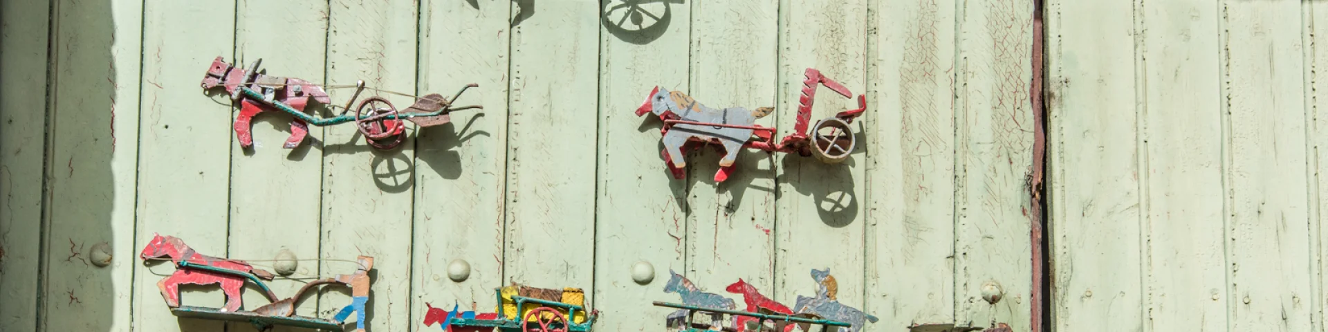 Décor mural original représentant des chevaux et des charrettes miniatures en métal peint, accrochés sur une porte en bois vert pâle.
