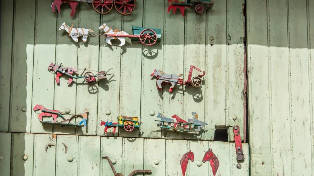 Décor mural original représentant des chevaux et des charrettes miniatures en métal peint, accrochés sur une porte en bois vert pâle.