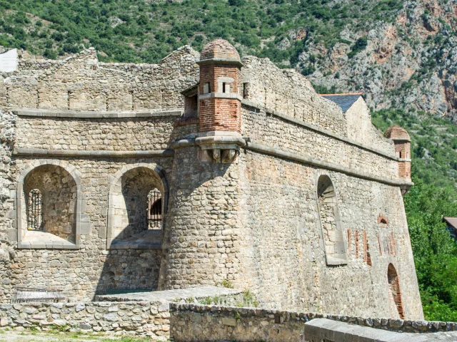 Détail des fortifications de Villefranche-de-Conflent, cité médiévale fortifiée classée au patrimoine mondial de l’UNESCO, avec ses bastions en pierre et briques rouges face aux montagnes verdoyantes du Conflent.