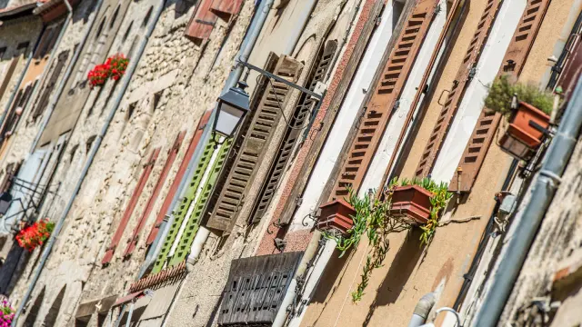 Détail des façades anciennes de Villefranche-de-Conflent, avec volets colorés, jardinières fleuries et lampadaires en fer forgé, sous le soleil catalan.