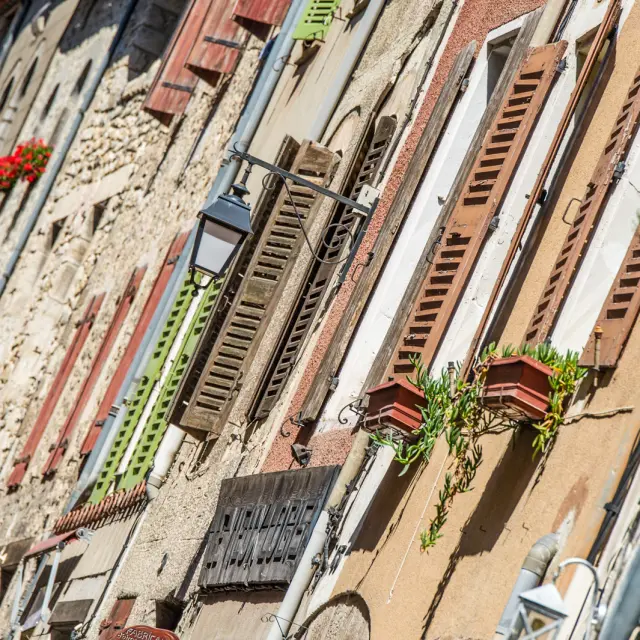 Détail des façades anciennes de Villefranche-de-Conflent, avec volets colorés, jardinières fleuries et lampadaires en fer forgé, sous le soleil catalan.