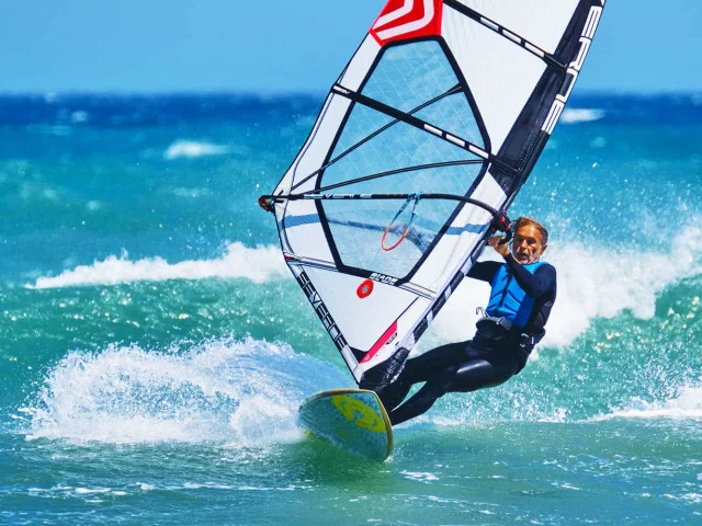 Planche à voile naviguant sur une mer turquoise agitée, sous un ciel bleu, portée par le vent de la Méditerranée.