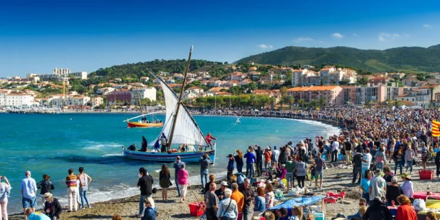 Grande foule rassemblée sur la plage de Banyuls-sur-Mer pour une fête traditionnelle avec barques catalanes à voile sur la mer.