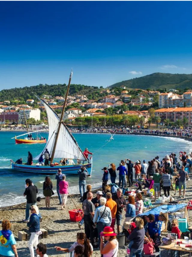 Grande foule rassemblée sur la plage de Banyuls-sur-Mer pour une fête traditionnelle avec barques catalanes à voile sur la mer.