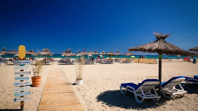 Plage aménagée de sable fin à Canet-en-Roussillon, avec transats, parasols en paille et promenade en bois menant jusqu’à la mer sous un ciel bleu éclatant.