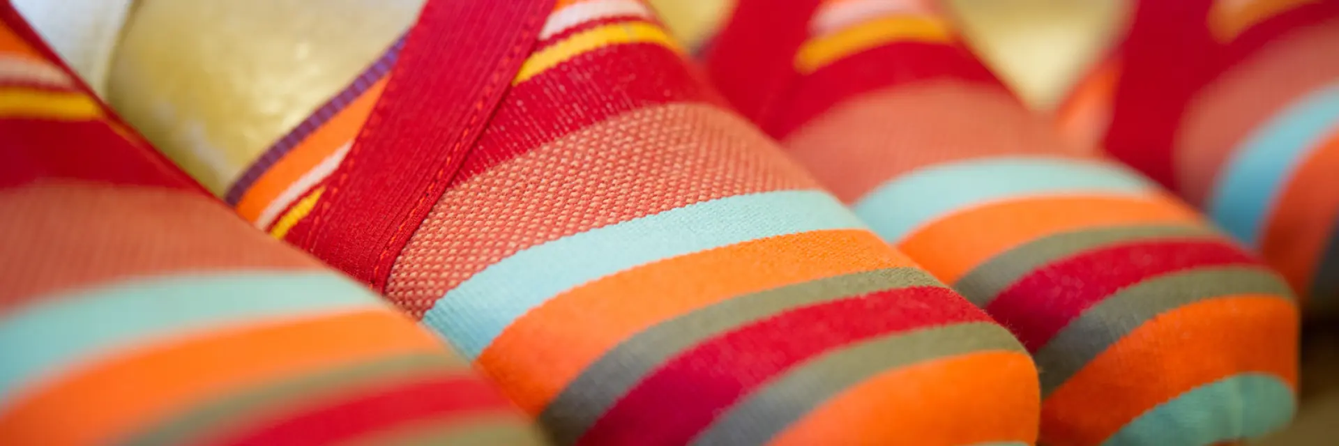 Espadrilles catalanes aux rayures colorées rouge, orange, turquoise et jaune, alignées sur une étagère.