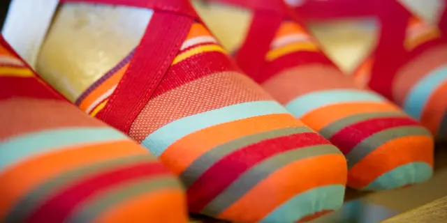 Espadrilles catalanes aux rayures colorées rouge, orange, turquoise et jaune, alignées sur une étagère.