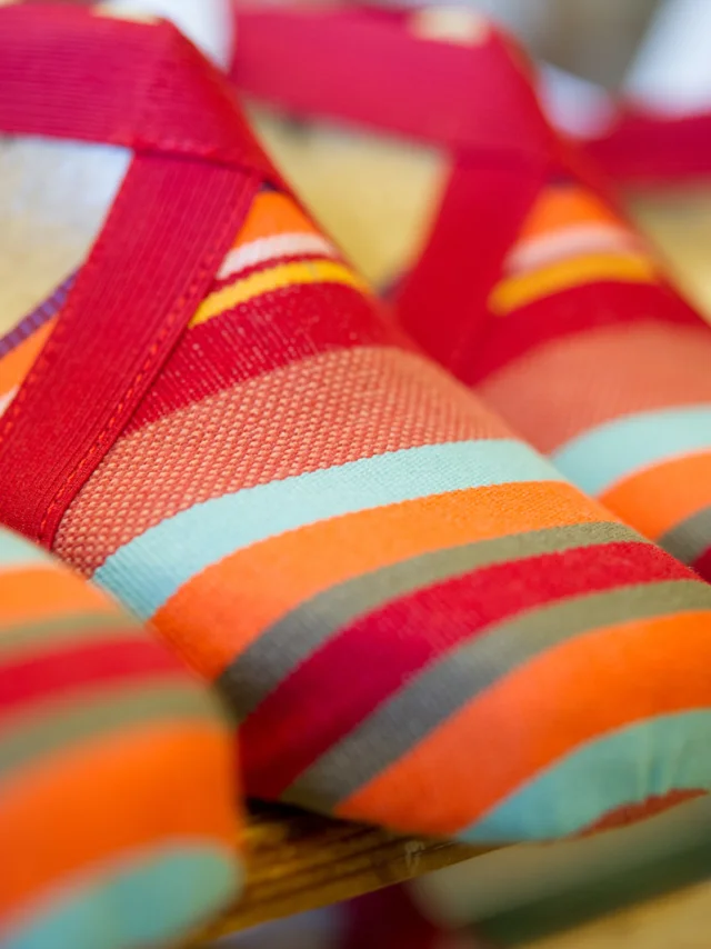 Espadrilles catalanes aux rayures colorées rouge, orange, turquoise et jaune, alignées sur une étagère.