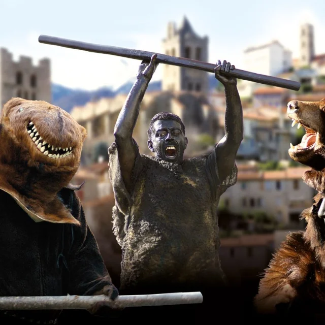 Personnages costumés incarnant la Fête de l’Ours dans un village des Pyrénées, avec des participants grimés et des costumes d’ours sur fond de clochers et de montagnes.