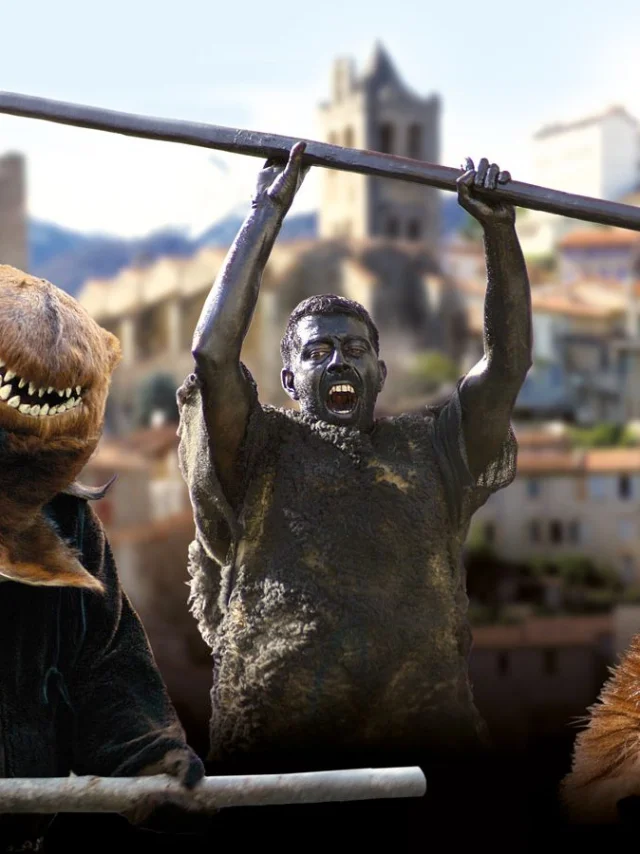 Personnages costumés incarnant la Fête de l’Ours dans un village des Pyrénées, avec des participants grimés et des costumes d’ours sur fond de clochers et de montagnes.