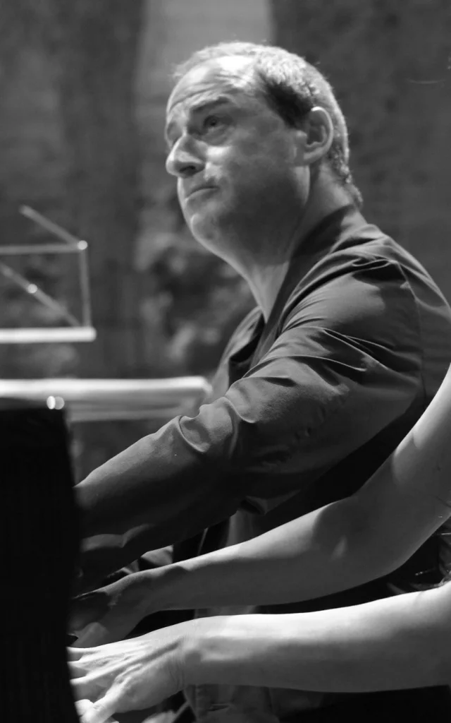 Deux pianistes jouant à quatre mains sur scène lors d’un concert, en noir et blanc.