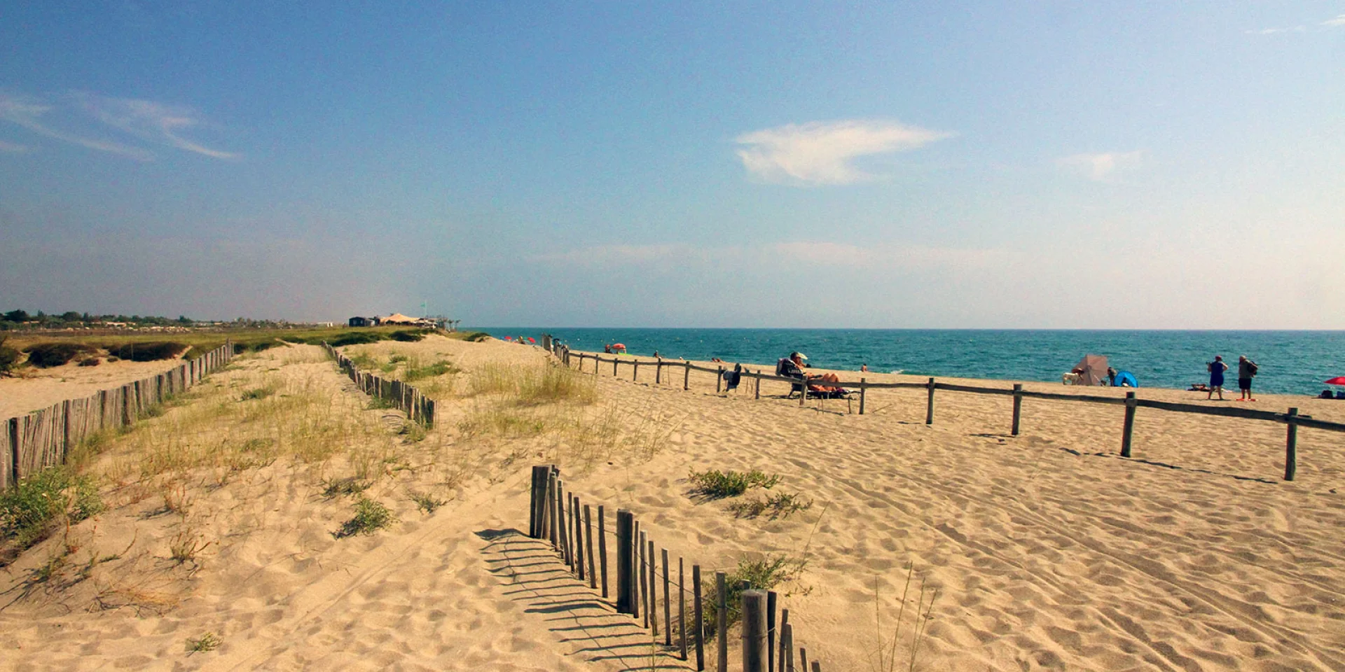 Plage naturelle de Torreilles bordée de dunes et de ganivelles en bois, avec quelques promeneurs et vacanciers face à la mer Méditerranée.