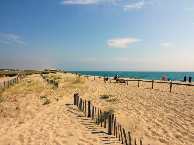 Plage naturelle de Torreilles bordée de dunes et de ganivelles en bois, avec quelques promeneurs et vacanciers face à la mer Méditerranée.