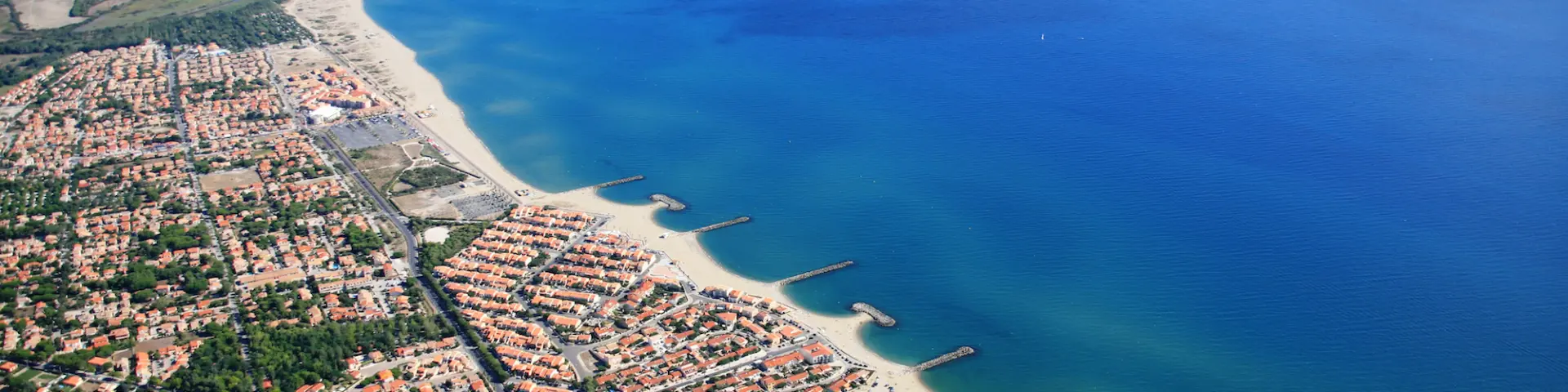 Vue aérienne du littoral des Pyrénées-Orientales avec la station balnéaire, la plage et le port de plaisance bordés par la Méditerranée.