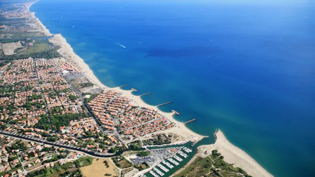Vue aérienne du littoral des Pyrénées-Orientales avec la station balnéaire, la plage et le port de plaisance bordés par la Méditerranée.