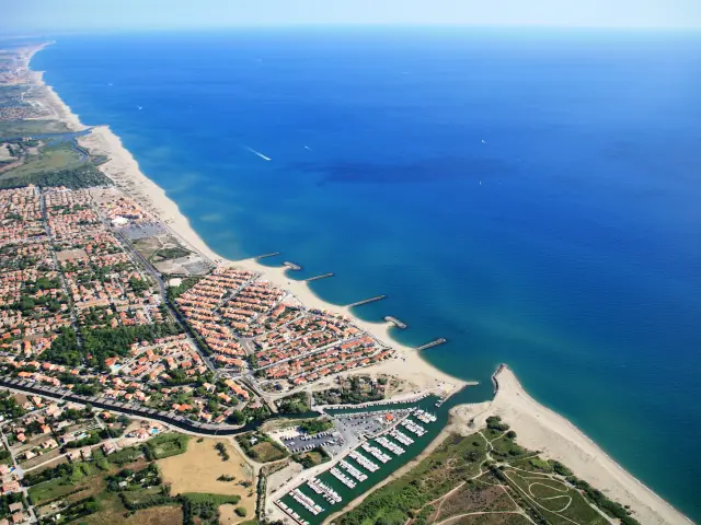 Vue aérienne du littoral des Pyrénées-Orientales avec la station balnéaire, la plage et le port de plaisance bordés par la Méditerranée.