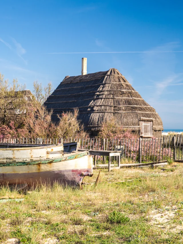 Cabanes traditionnelles en roseaux bordées d’une barque en bois, sur fond de mer bleue et de ciel clair.