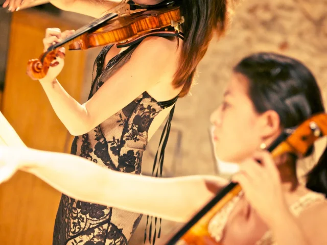 Deux musiciennes interprétant une œuvre classique, l’une au violon et l’autre au violoncelle, dans une salle voûtée.