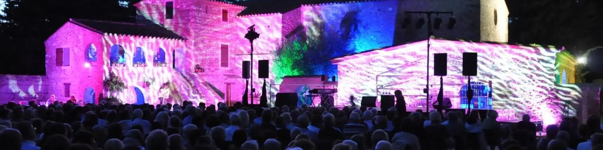 Spectacle nocturne en plein air projeté sur les façades illuminées d’un bâtiment en pierre, devant un public rassemblé dans les Pyrénées-Orientales.