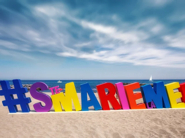 Installation colorée en forme de lettres géantes formant le mot « #STEMARIELAMER » sur la plage de Sainte-Marie-la-Mer, face à la Méditerranée.